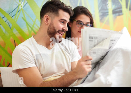 Lächelnden jungen Menschen Zeitung lesen im Bett Stockfoto