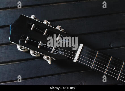 Schwarz Akustik Gitarre Kopf, Stimmwirbel, Mutter und Streichern, Holz Tisch auf einem schwarzen Hintergrund, mit vielen Texturen Hintergrund und Leitungen Stockfoto