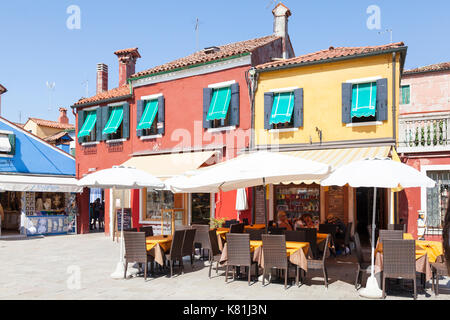 Bunte open air Restaurant Burano, Venedig, Italien mit ein paar Touristen sitzen Essen in einem kleinen Platz mit Geschäften Stockfoto