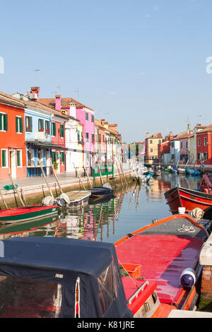 Bunte rote, Arbeit Boote bei Sonnenaufgang in einem Kanal auf Burano, Venedig, Venetien, Italien, gesäumt mit bunt bemalten Häuser im Wasser unter. Stockfoto