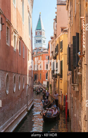 Die Gondolieri rudern Gondeln durch einen sehr schmalen Kanal, in San Marco, Venedig, Italien mit dem Campanile von San Marco Basilika hinter Ihnen aus gesehen Stockfoto