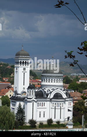 Dreifaltigkeitskirche mit rumänischer Flagge und wolkenverirlter Himmel. Sighisoara, Siebenbürgen, Rumänien Stockfoto