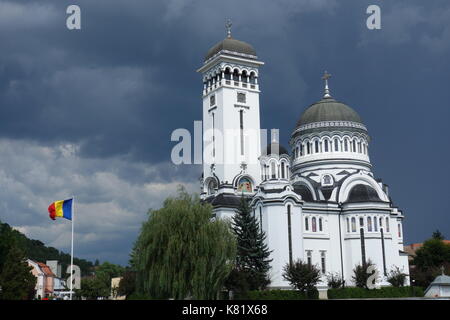 Dreifaltigkeitskirche mit rumänischer Flagge und wolkenverirlter Himmel. Sighisoara, Siebenbürgen, Rumänien Stockfoto