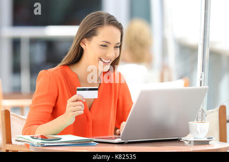 Einzige Frau in orange Bezahlung Online mit Kreditkarte und einen Laptop in einem Restaurant sitzen Stockfoto