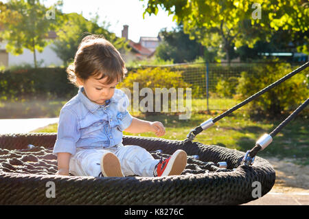 Verspielte Junge sitzt auf einem runden Swing im Park Stockfoto