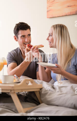 Glückliches junges Paar mit Frühstück im Bett Stockfoto
