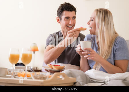 Glückliches junges Paar mit Frühstück im Bett Stockfoto