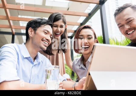 Gruppe von vier jungen asiatischen Menschen sitzen zusammen im Freien an einem Stockfoto