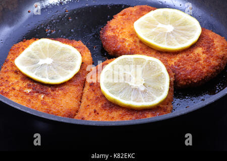 Schnitzel in der Pfanne knusprig gebratern mit Zitrone, Schnitzel in einer Pfanne knusprig gebraten mit Zitrone Stockfoto
