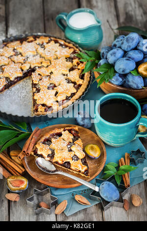 Hausgemachte, traditionelle Pflaumenkuchen mit cinamon und Mandeln mit Kaffee auf alten hölzernen Hintergrund Stockfoto