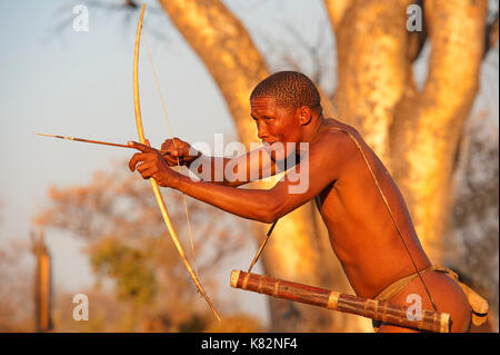 Ju/'Hoansi oder San Buschmänner Hunter simuliert eine Jagd mit Pfeil und Bogen in seinem Dorf. Sie sind Mitglieder der verschiedenen indigenen Jäger-sammler Volk Stockfoto