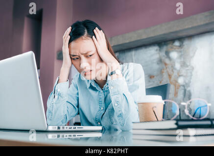 Asiatische Geschäftsfrau, die ihr Gesicht mit der Hand und Depression über die Arbeit in der Laptop auf dem Schreibtisch im Büro, Druck im Amt betonte Stockfoto