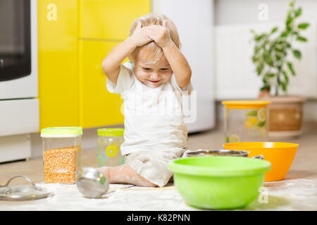 Spielendes Kind Kleinkind mit Gesicht verschmutzt Mehl. Kleiner Junge umgeben, Geschirr und Lebensmittel Stockfoto