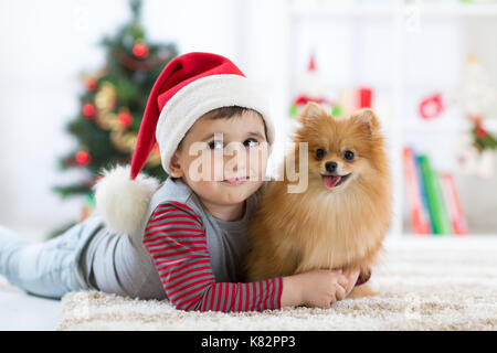 Kleiner Junge und Hund am Weihnachtsbaum liegen Stockfoto