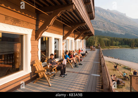 Gäste des Swiftcurrent Lodge Sitzen auf dem Balkon mit Blick auf den See und genießen den Sonnenuntergang auf den warmen Sommerabend Stockfoto