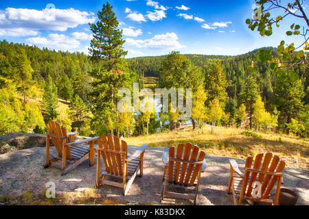 Adirondack Stühle arainged auf einem Felsen mit Blick auf die Berge und den See im Herbst. Stockfoto