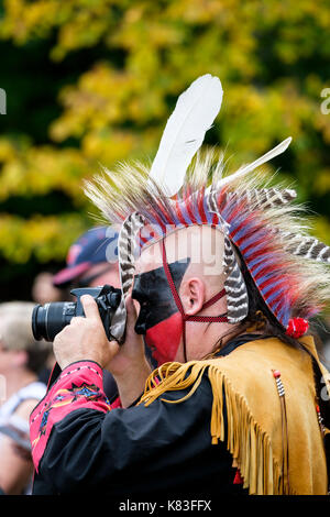 Kanadische indigene, männliche Wahta Mohawk/Irokesen-Kriegerin, die eine digitale Spiegelreflexkamera verwendet, um ein Pow Wow-Treffen in London, Ontario, Kanada, zu fotografieren. Stockfoto