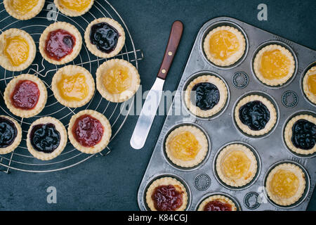 Zubereitet hausgemachte Marmeladentörtchen in einem Backblech und auf einem Vintage kreisförmigen Gitter Stockfoto