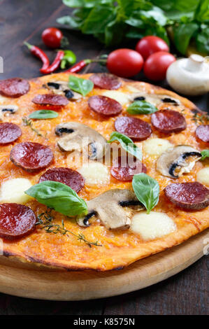 Leckere italienische Pizza mit Salami, Champignons, Mozzarella, Basilikum auf einem dunklen Holztisch. Ansicht von oben. Stockfoto