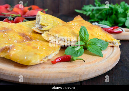 Khachapuri mit Fleisch - Traditionelle georgische Gebäck auf einem dunklen Holztisch. Stockfoto