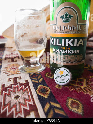 In der Nähe der Armenischen Kilikia Bier Flasche und einen fast leeren Glas auf eine gewebte Tischdecke mit traditionellen Muster, Mittagessen im Dorf Garni, Armenien Stockfoto