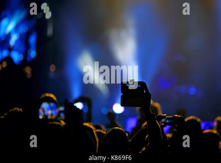 Fans, die Bilder und Videos mit modernen Smartphones während des Live Konzert einer Rockband auf der Bühne nehmen Stockfoto