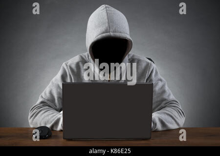 Hacker in der Kapuze Jacke mit Laptop am Tisch Stockfoto