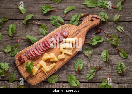 Käse und Salami auf Küche Board auf rustikalen Hintergrund. Ansicht von oben mit der Kopie Raum und Kräutern. Stockfoto