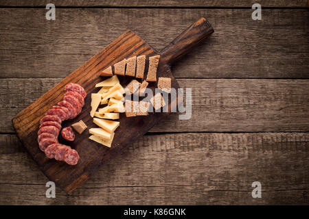 Schneidbrett mit Salami, Käse und Brot auf dunklem Hintergrund Stockfoto