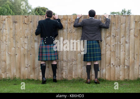 Zwei Männer in Kilts peeking über einen Gartenzaun Stockfoto