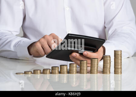 Mittelteil der Geschäftsmann mit Taschenrechner mit gestapelte Münzen im Büro Schreibtisch angeordnet Stockfoto