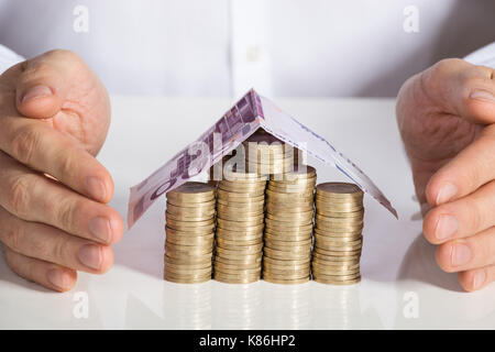 Mittelteil der Geschäftsmann schutz Haus von Münzen und Banknoten am Büro Schreibtisch gemacht Stockfoto