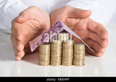 Mittelteil der Geschäftsmann schutz Haus von Münzen und Banknoten am Büro Schreibtisch gemacht Stockfoto