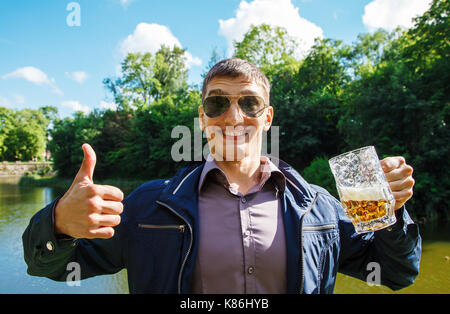 Fröhlich lächelnd Mann hält einen großen bierkrug und Daumen hoch im Freien Nahaufnahme Stockfoto