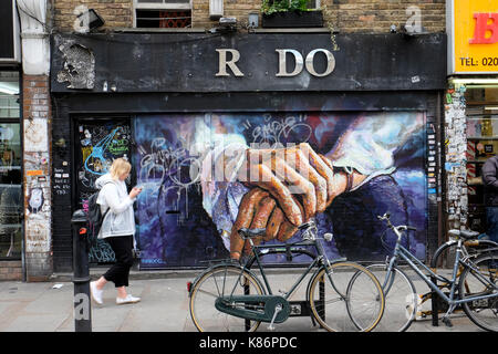 Eine Frau geht über einen leeren Laden, in Graffiti bedeckt, Brick Lane, London. Stockfoto