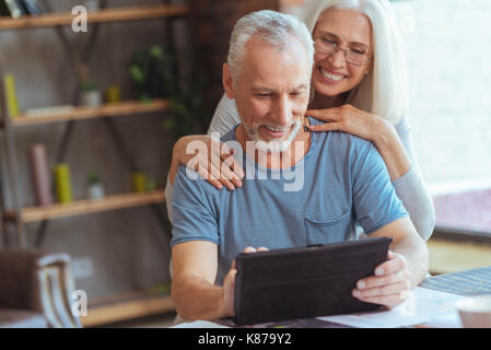 Positiver Mann mit Tablet mit seiner Frau zurückgezogen Stockfoto