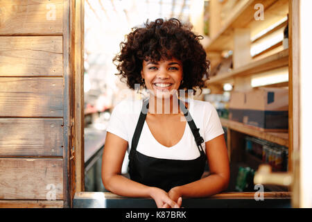 Frau barista in Ihr Coffee Shop. Curly behaarte Frau Barkeeper in fröhlicher Stimmung hinter der Theke. Stockfoto