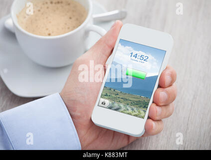 Nahaufnahme einer Hand, die das Mobiltelefon mit geladenem Akku auf einem Bildschirm Stockfoto