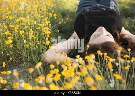 Eine Frau in einem schwarzen Weste Top und Jeans, die auf dem Gras mit ihren Händen hinter dem Kopf. Stockfoto