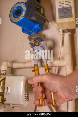 Ein Klempner in einem Trockenschrank arbeiten, können Sie über einen verstellbaren Schraubenschlüssel, auf eine defekte Heizungspumpe zu arbeiten. England, UK. Stockfoto