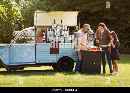 Der bärtige Mann mit Schürze, Frau und Mädchen stehend von Blue mobile Coffee Shop. Stockfoto