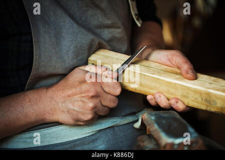 Nahaufnahme eines Handwerkers und schneiden Sie die Ecken eines Stück Holz mit einem scharfen Schnitzmesser. Stockfoto