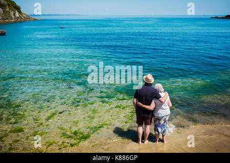 Ansicht der Rückseite des älteren Paares stehend mit Arme um einander über den strahlend blauen und türkisfarbenen Wasser suchen, das Meer. Stockfoto