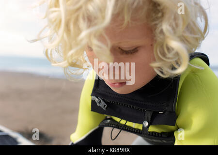 Junge Junge, bereit zum Surfen mit seinem Surfbrett am Strand das Tragen von Neoprenanzug an einem Sommertag. Stockfoto