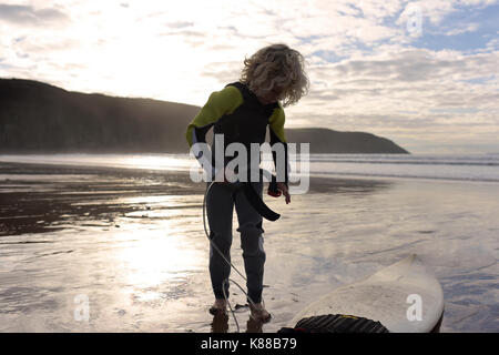 Junge Junge, bereit zum Surfen mit seinem Surfbrett am Strand das Tragen von Neoprenanzug an einem Sommertag. Stockfoto