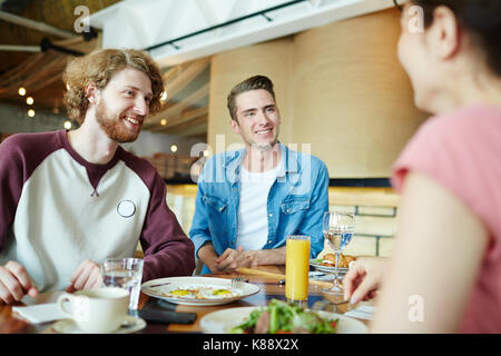 Fröhliche Gruppe von Freunden genießen jede andere Firma beim zusammen in der gemütlichen kleinen Café versammelt, Sie köstliches Essen und unterhalten sich angeregt wi Stockfoto