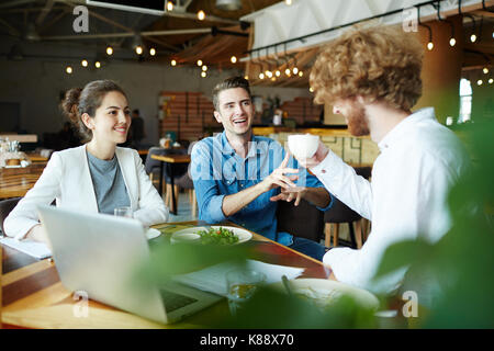 Multi-ethnischen Team junger Manager analysieren der Ergebnisse der durchgeführten Arbeiten mit Hilfe von Laptop beim Mittagessen im gemütlichen Cafe Stockfoto