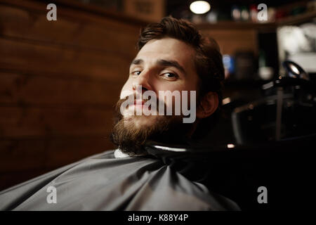 Junger bärtiger Mann bereit für die Haare schneiden oder rasieren an der Kamera in Haarpflege salon suchen Stockfoto