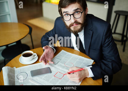 Verwirrt Mann mit Kamera beim Markieren neugierig Vakanz Werbung in Zeitung Stockfoto
