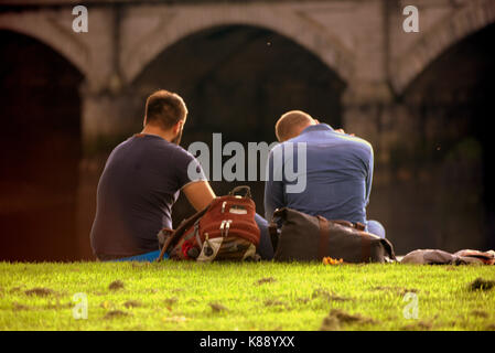 Touristische Paare sitzen auf dem Gras am Ufer des Flusses Clyde Glasgow Schottland Stockfoto